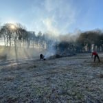 Volunteers clearing dead growth off a field with a small fire burning on a frosty sunny morning