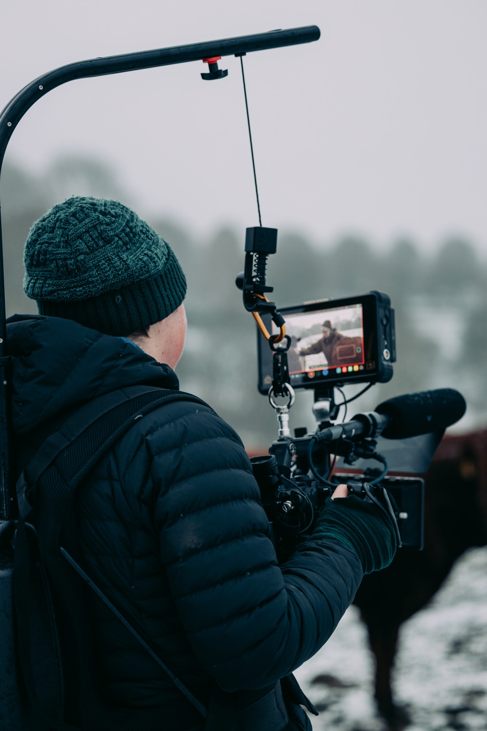 Image shows a person holding professional filming equipment, filming outside in the snow.
