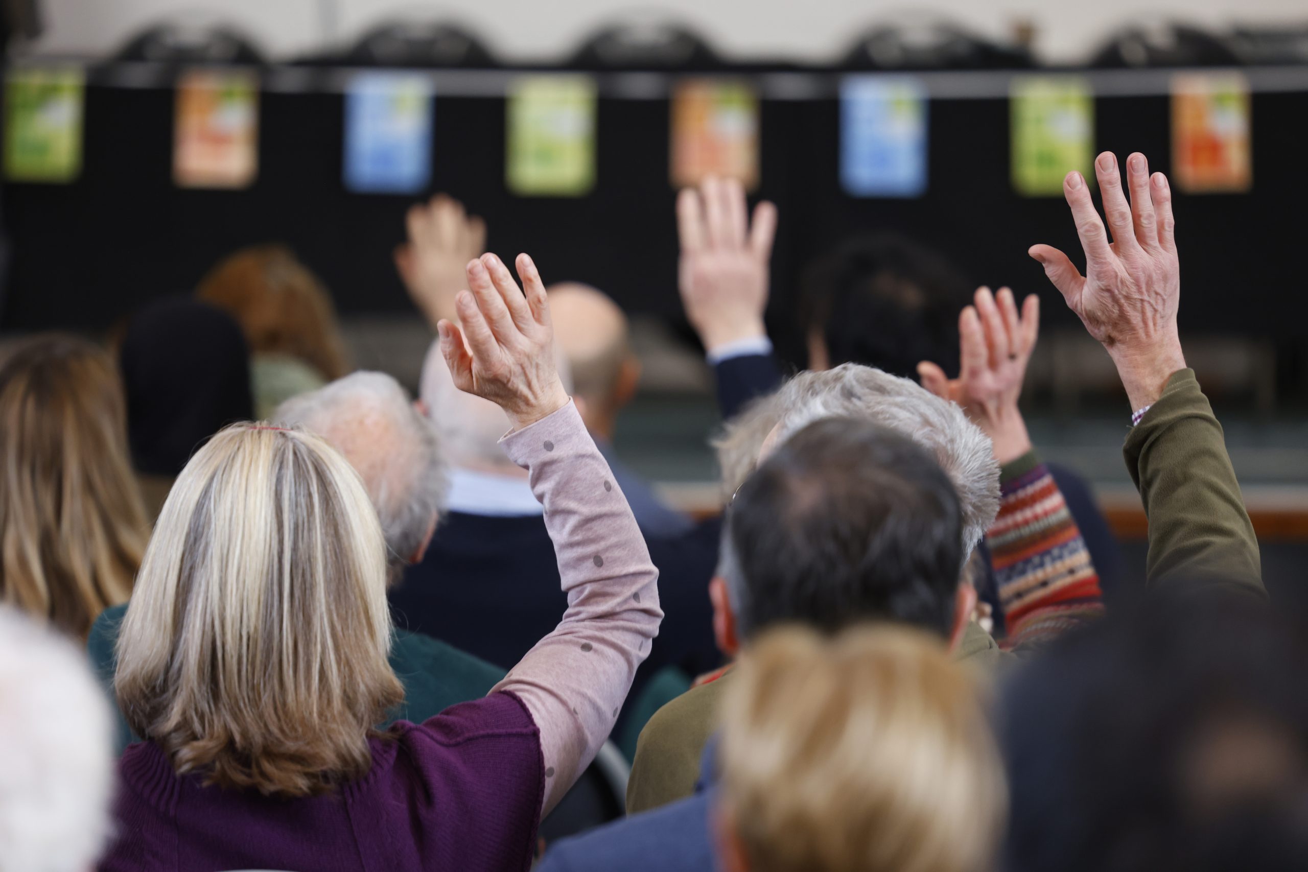 Image shows a conference room full of people - some have their hands up to ask a question.