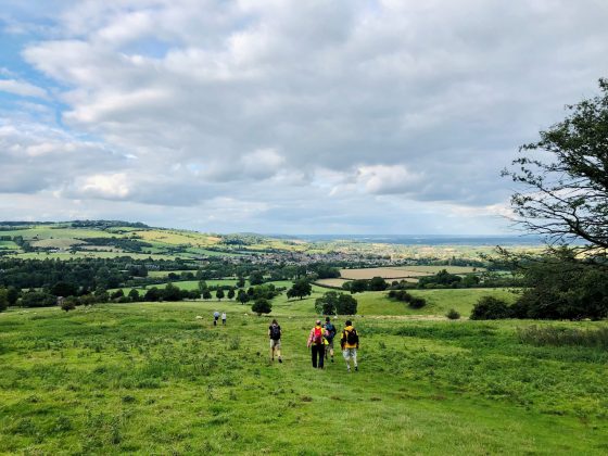 Image shows a group of people walking downhill through a field to the town of Winchcombe.