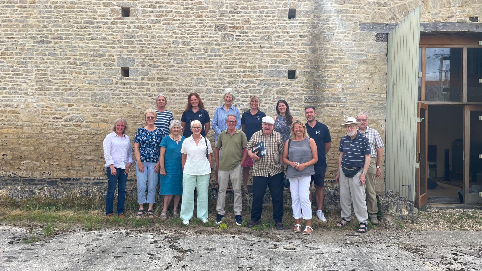 Image shows a group of smiling people standing in front of a stone barn.