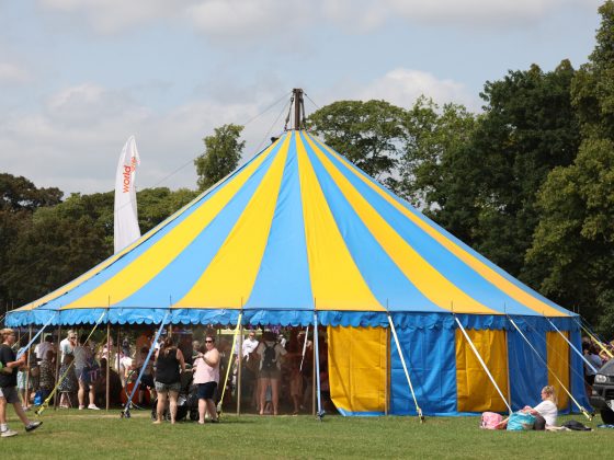 Image is a photo of a blue and yellow big top tent with people going in and out.